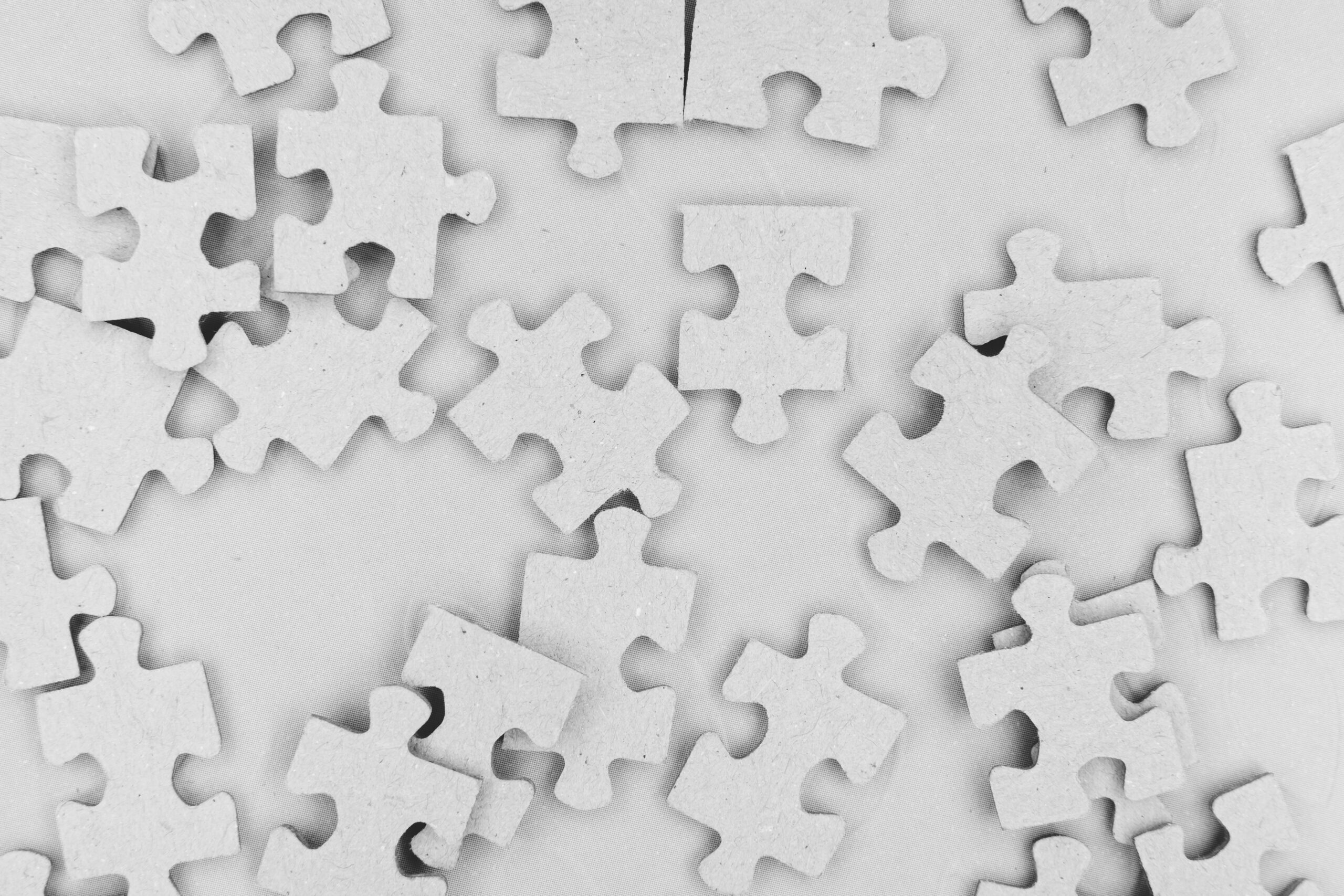 Several scattered, unassembled jigsaw puzzle pieces lie on a flat, light-colored surface. The pieces are beige and have various edge shapes, suggesting an unfinished puzzle.