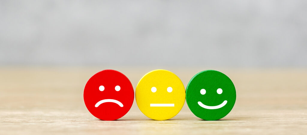 Three round wooden tokens in a row showing a red frowning face, a yellow neutral face, and a green smiling face.