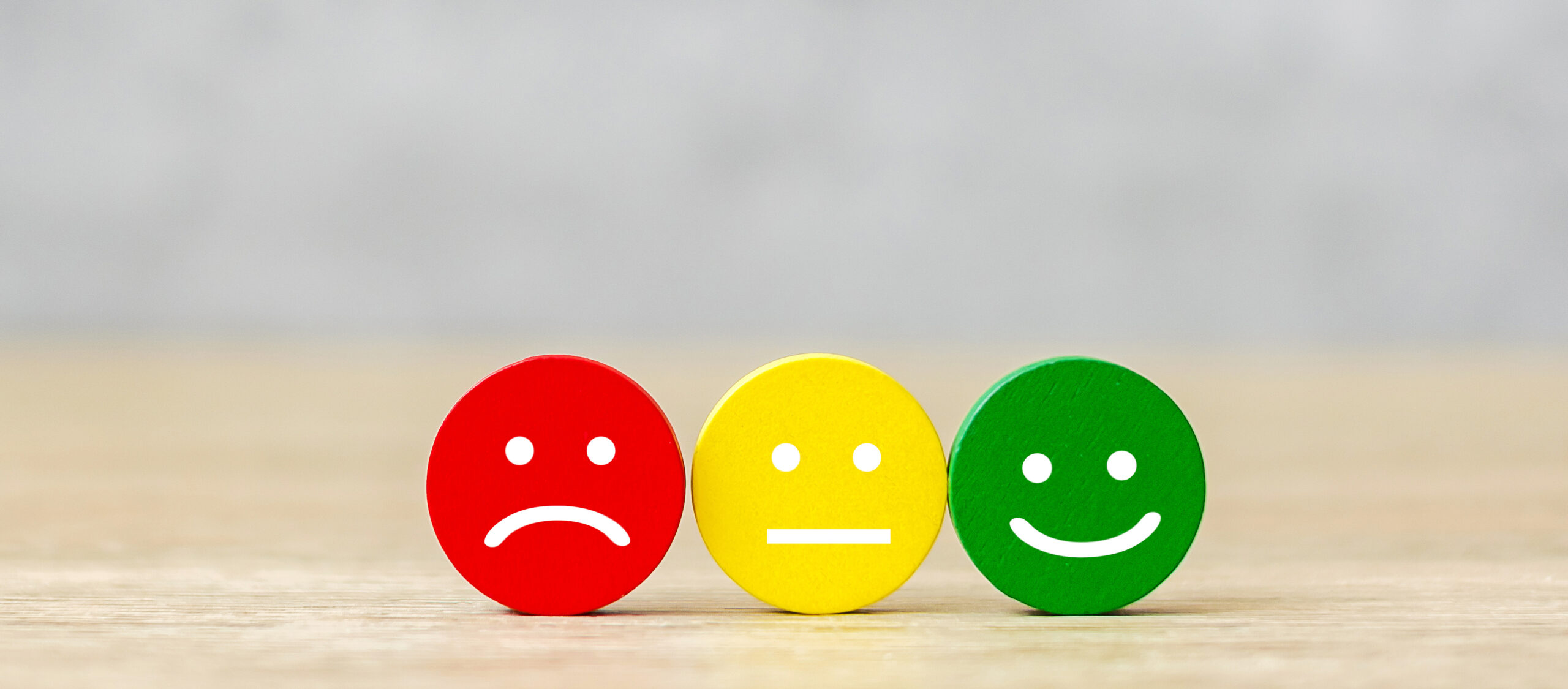 Three round wooden tokens in a row showing a red frowning face, a yellow neutral face, and a green smiling face.